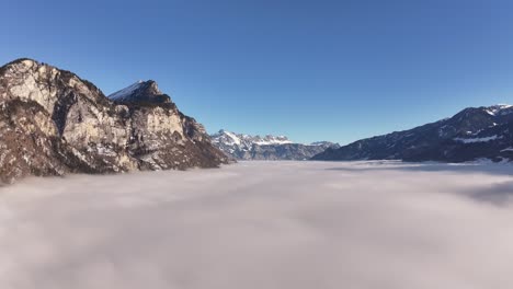 aerial - walensee switzerland covered in thick fog with towering swiss alps and clear sky