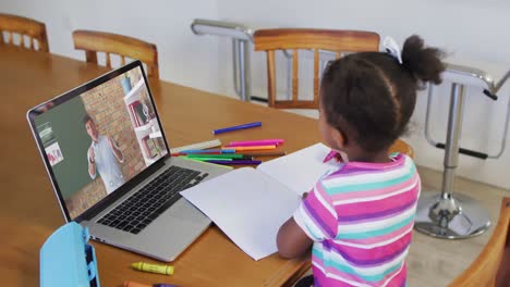 African-american-girl-doing-homework-while-having-video-call-with-male-teacher-on-laptop-at-home