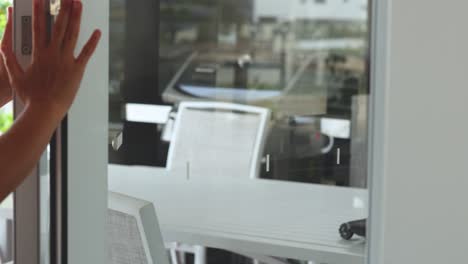a woman in a light pink shirt opens a modern sliding glass door, revealing a bright outdoor patio with white furniture in natural daylight