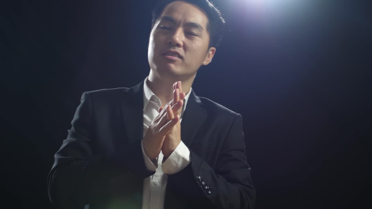 블랙 스크린 스튜디오에서 말하는 동안 손을 함께 잡고 지표손가락을 보여주는 비즈니스 슈트를 입은 아시아 스피커의 클로즈업