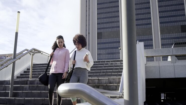 Diverse amiche scendono le scale esterne, trasportando borse da palestra, ridendo dopo aver bevuto acqua
