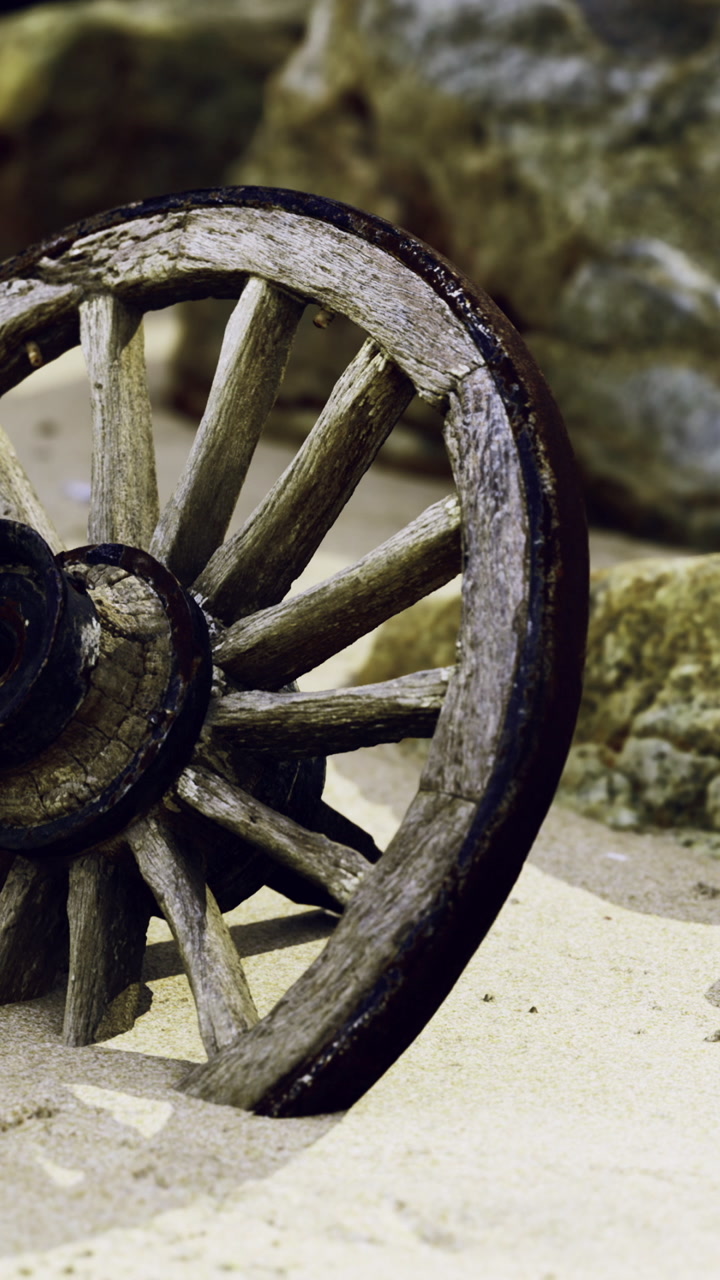 Wooden wheel rests on sandy ground near rocks at coastal location