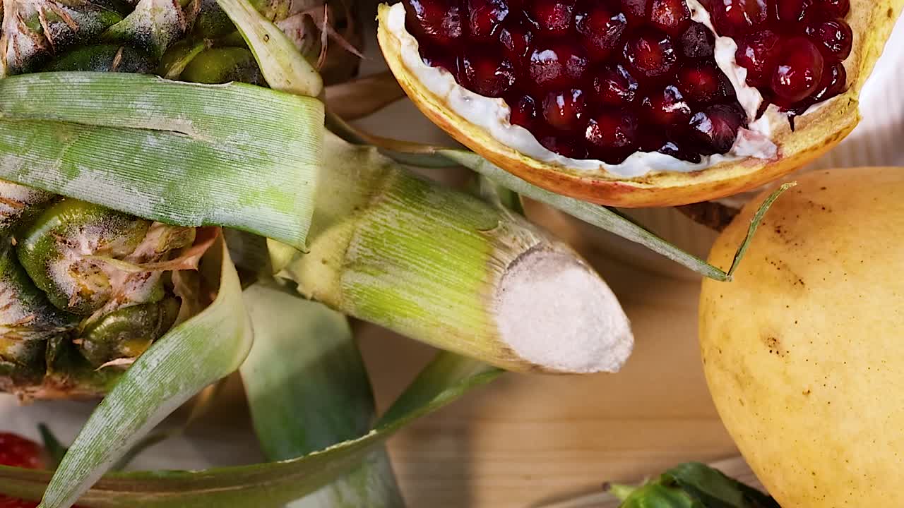 A colorful display of strawberries, pineapples, pomegranates, papayas, bananas, and melons on a wooden surface.