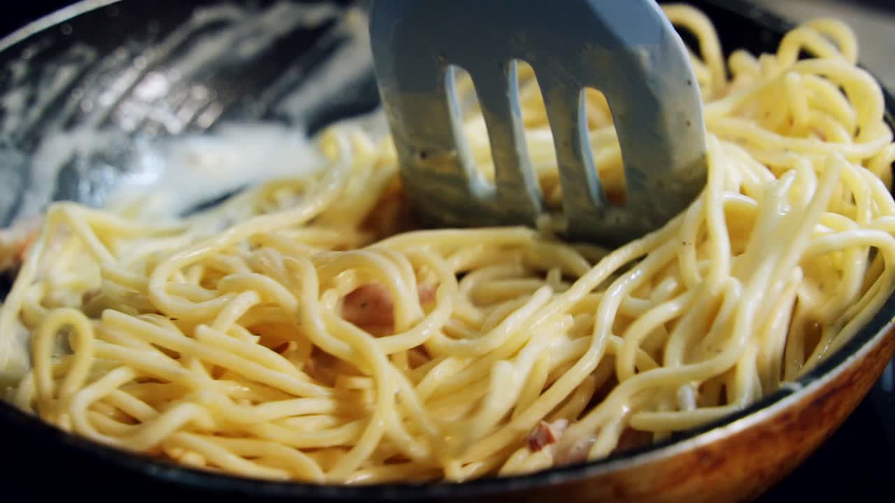 Cooking and stirring the spaghetti with white sauce in the frying pan. Chef mixes ready-made spaghetti pasta with a spatula . Preparing food in a restaurant. Close-up
