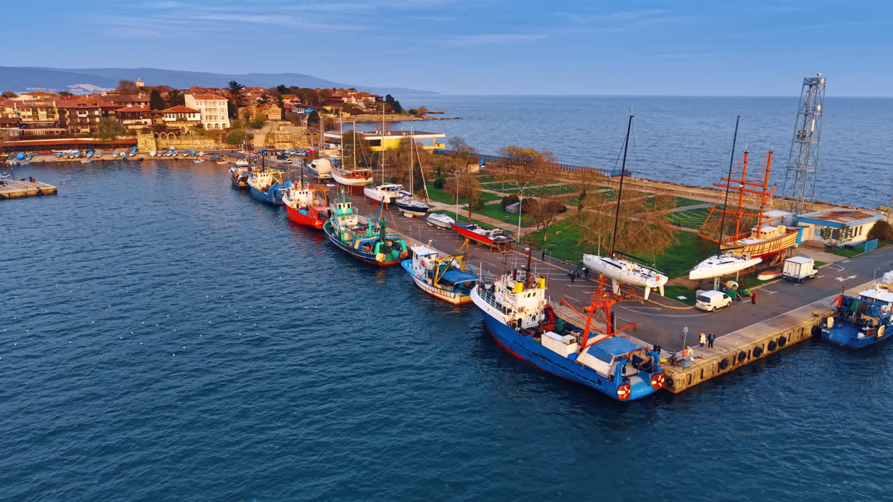 Barche da pesca e yacht al molo circondati dalle acque azzurre. Prospettiva aerea sul paesaggio urbano di Nesebar, Bulgaria, al tramonto