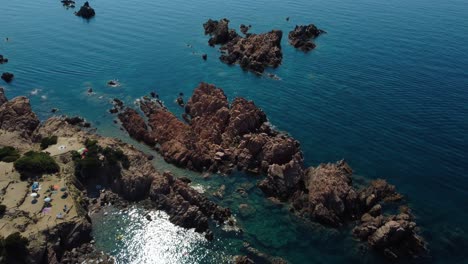 Aerial-of-a-natural-coast-beach-rock-sandy-bay-on-the-tourist-vacation-island-Sardinia-in-Italy-with-sun,-clear-blue-turquoise-and-calm-water-close-to-Capo-Testa