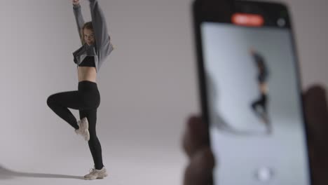 person recording video on mobile phone of woman doing dance practise on grey background in studio 1