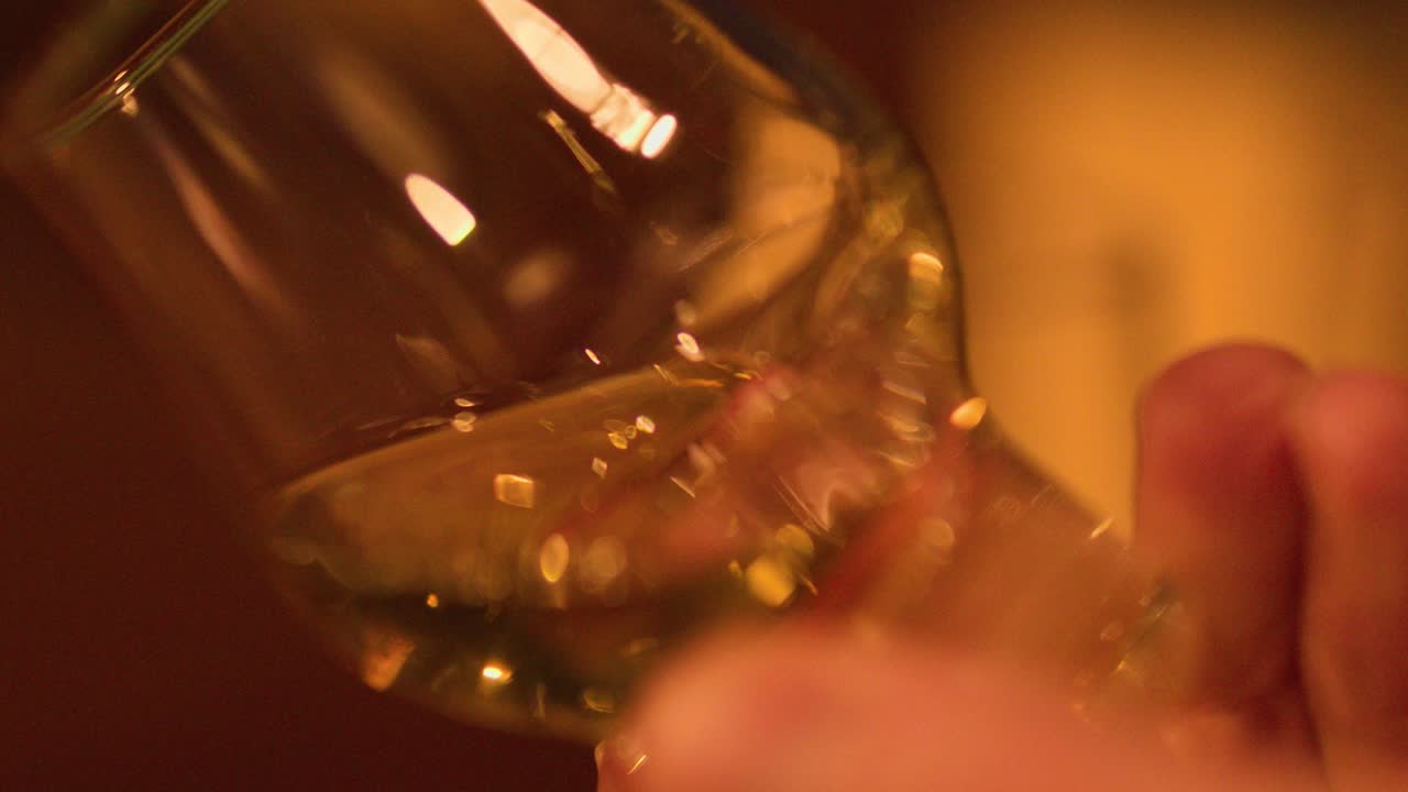 Hand gently swirls whisky glass, golden liquid illuminated by soft, ambient distillery lighting
