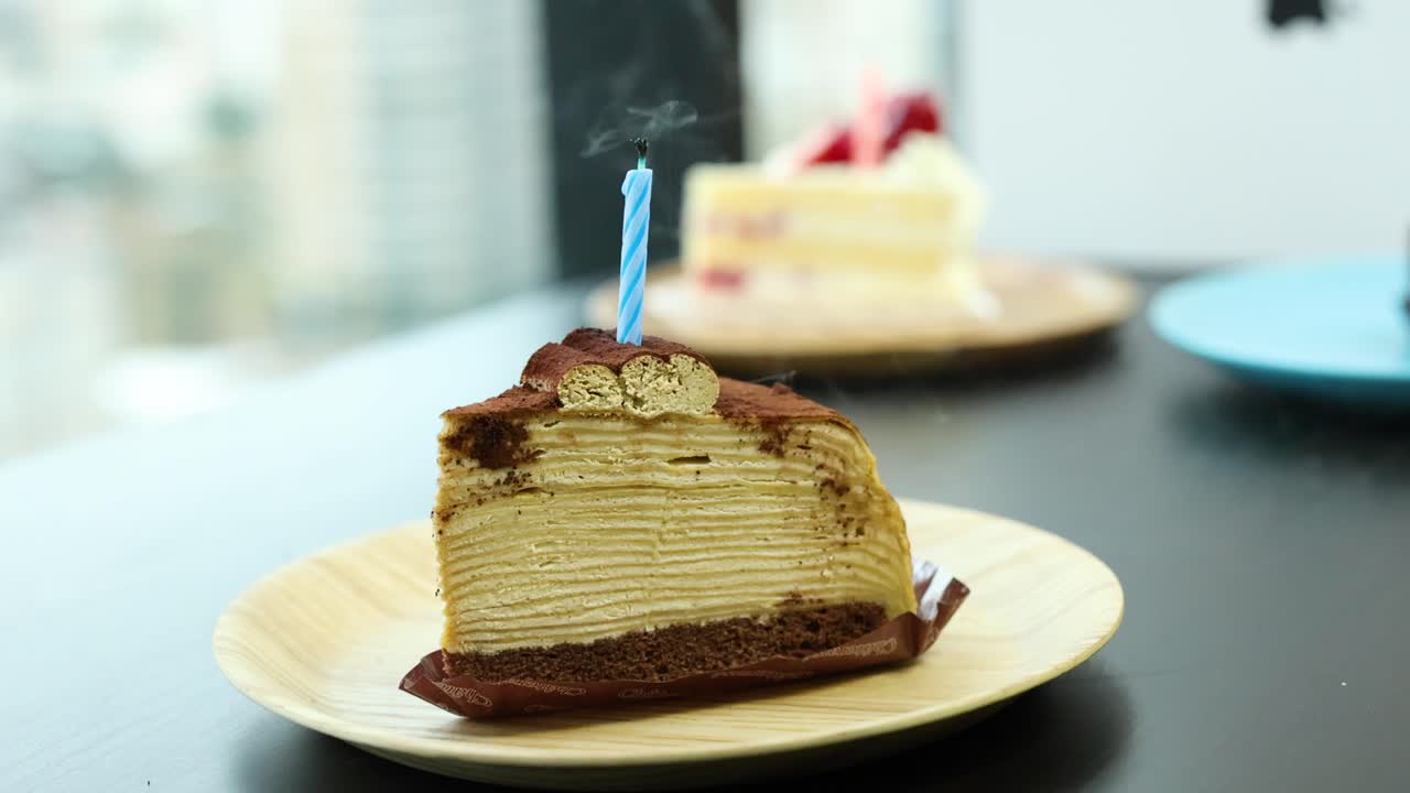 Single blue candle extinguished on tiramisu crepe cake slice, natural daylight, shallow depth