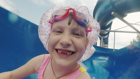 a cool girl in a pink swimsuit and pink glasses goes down from the water slide in the water park hap