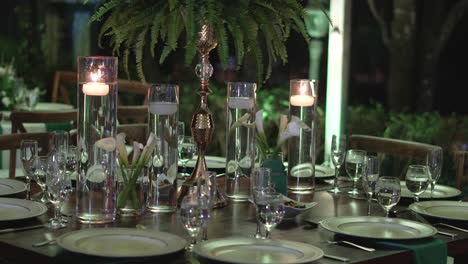 mesa decorada con piezas centrales de follaje natural y artículos de vidrio para la recepción de bodas