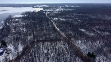 aerial shot moving forward over a forest in winter following a car on the road