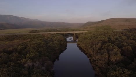 arroyo ribereño con puente y montañas