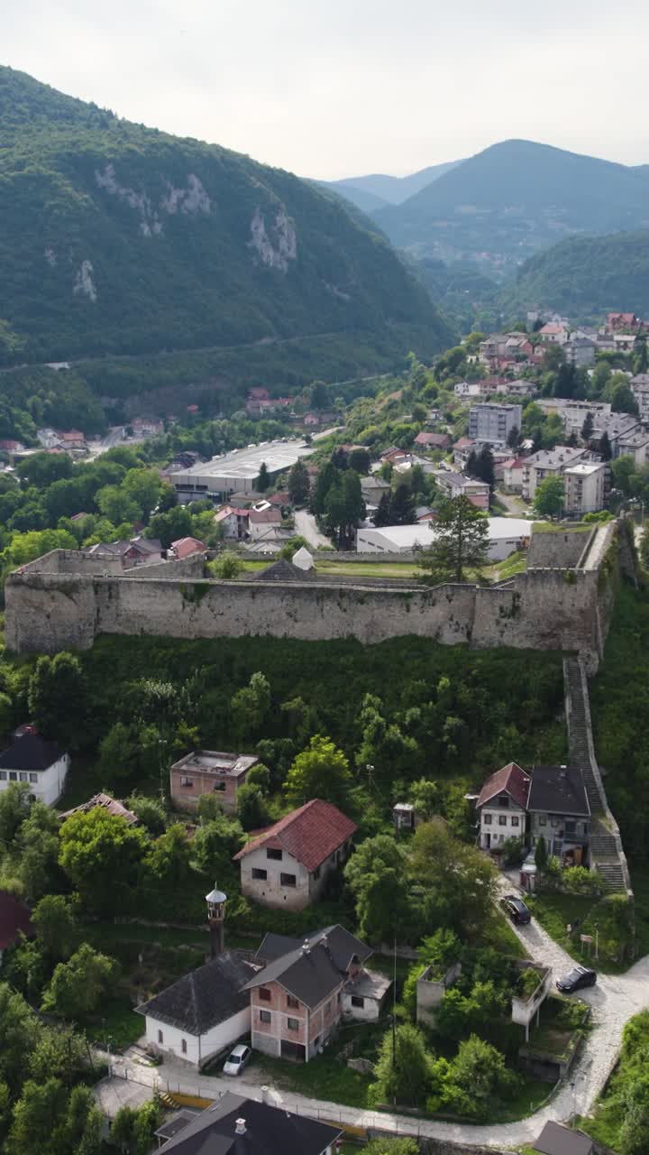 Scenic aerial view of Jajce Fortress amidst lush greenery and a historic town. Vertical Video, Orbit Motion