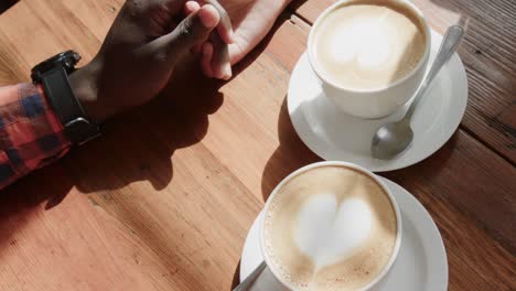 close up of african american couple holding hands at table with coffees in coffee shop, slow motion