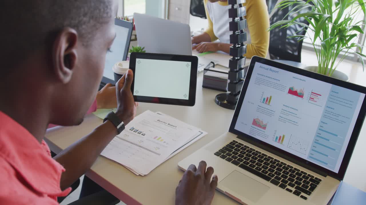 African american businessman at desk, reading report, using laptop and tablet with copy space