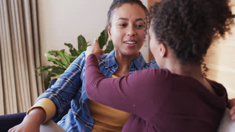 Romantic-biracial-lesbian-couple-relaxing-on-couch-together,-smiling-and-talking,-in-slow-motion