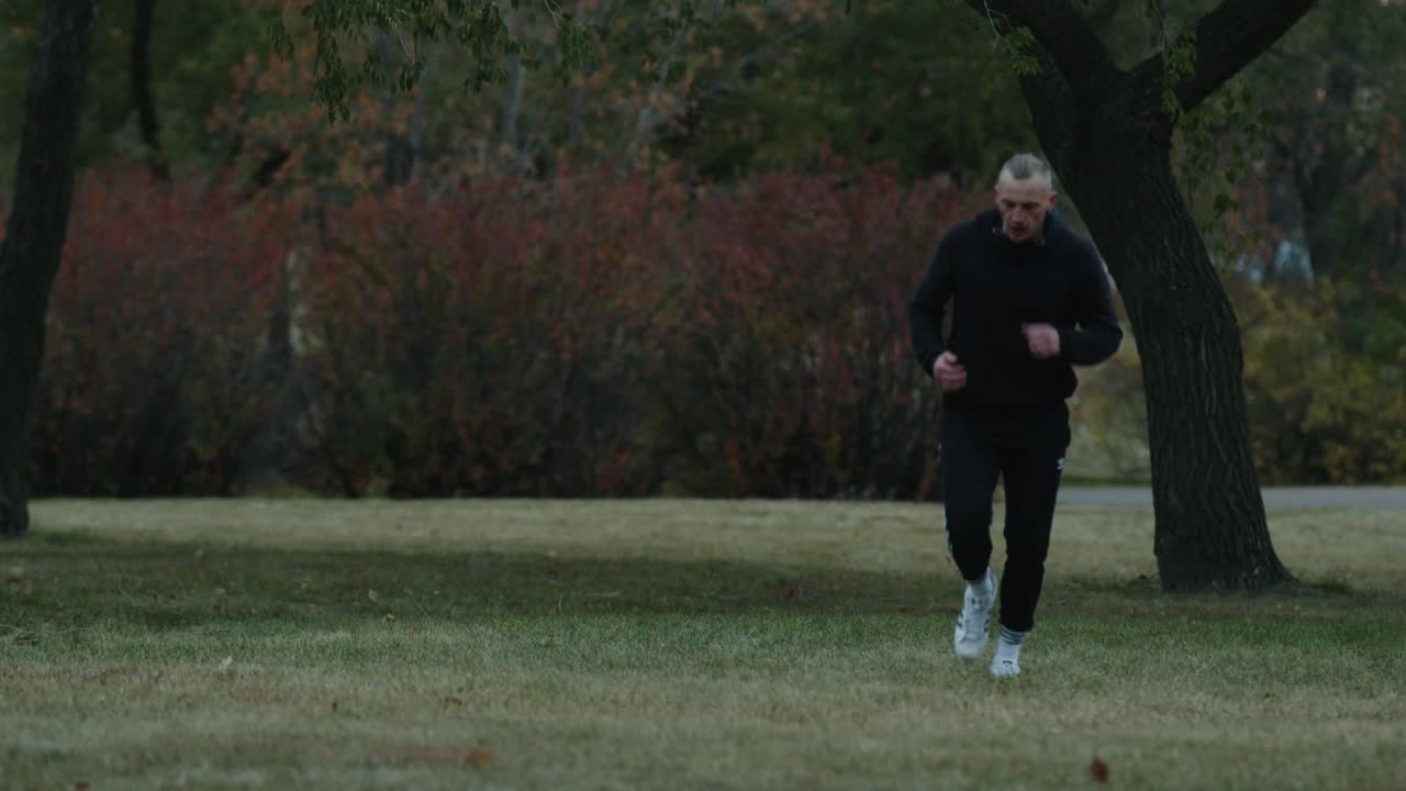 남자 운동 선수 가 운동복 을 입고 잔디 에 있는 공원 을 가로질러 달리고 있다