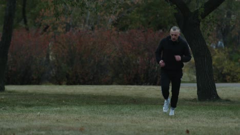male athlete running through park on the grass wearing a tracksuit