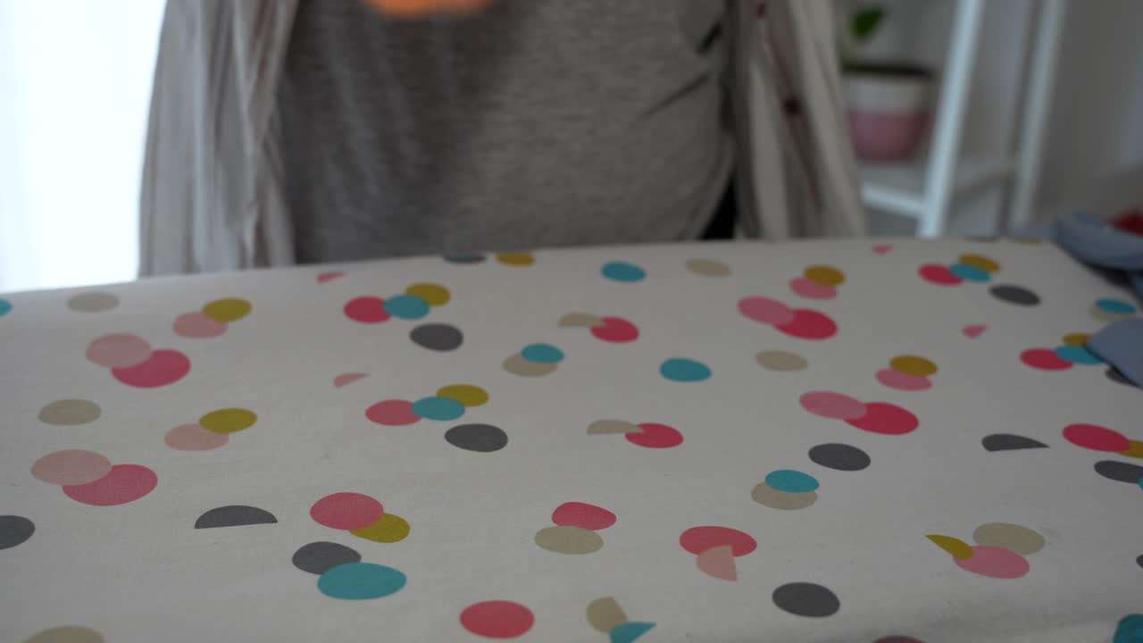 Woman folding baby bodysuit after ironing, fastening snaps on soft orange fabric