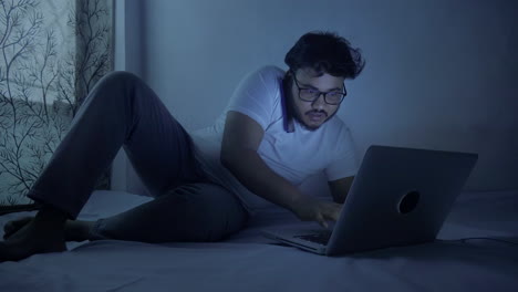 indian-man-wearing-casual-outfit-talking-on-mobile-phone-while-typing-on-laptop-keyboard-at-home-during-late-night