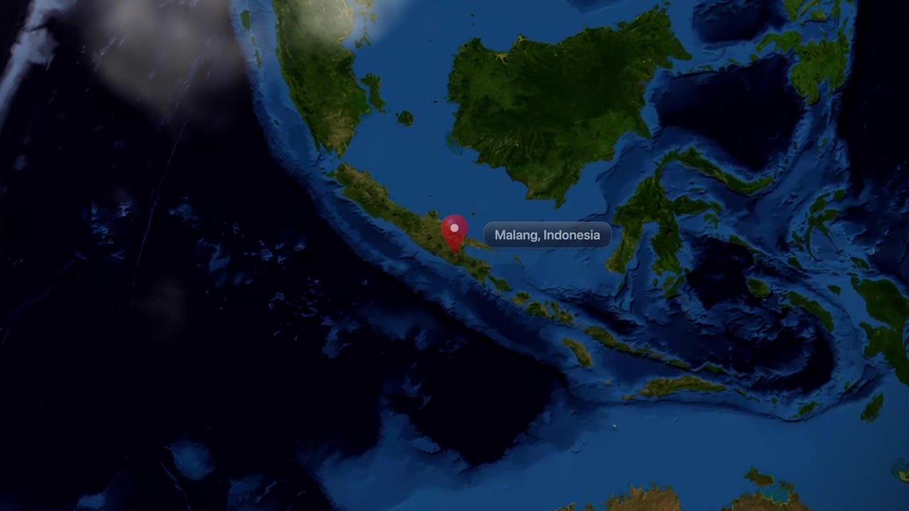 Satellite view camera zooms in from space to pinpoint Malang, Indonesia with pin marker. Includes NASA public domain imagery.