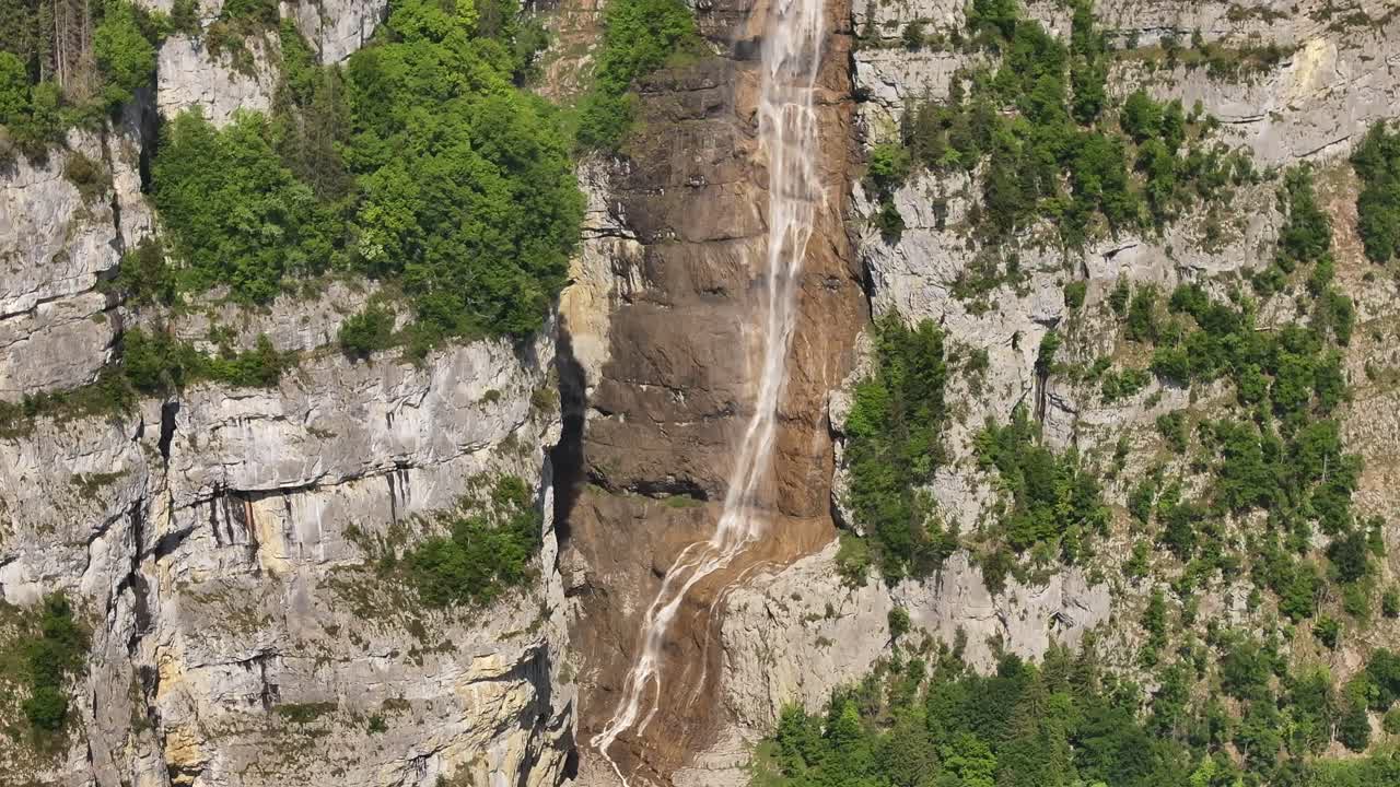 Seerenbach Falls spills from rugged alpine cliffs into a deep green valley, framed by dense forests and dramatic rocky terrain in the Swiss landscape