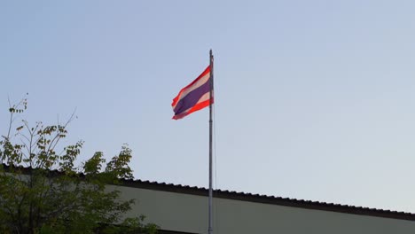 thai flag waving on top of roof against blue sky in slow motion