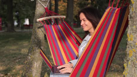 woman working on a laptop in a hammock in a park