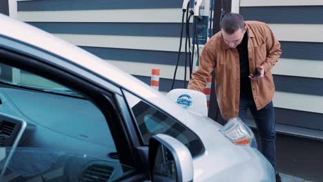 refueling process of an electric car. a shot under the hatch where the electric eco car charges. the electric car charging hatch opens automatically. a male hand inserts an erectile car