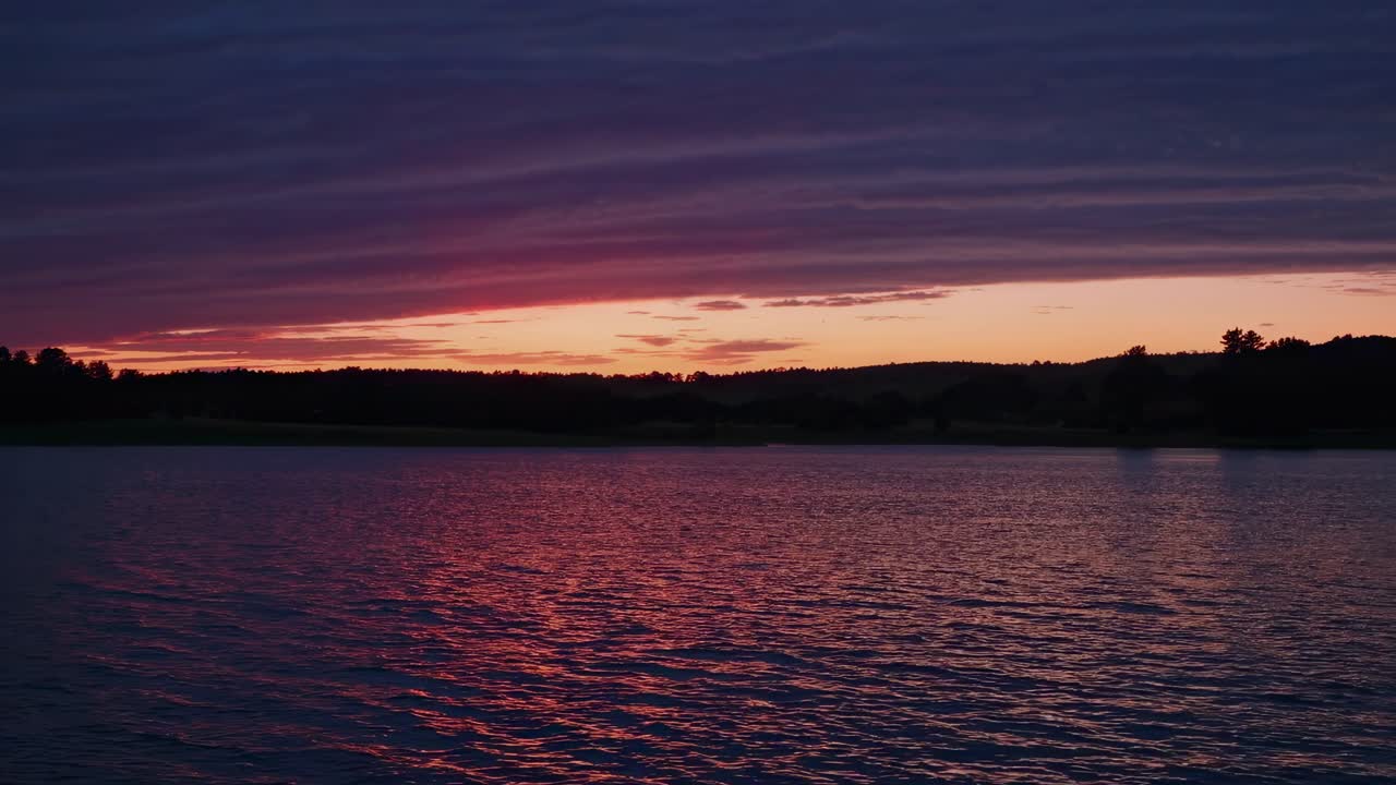 A serene sunset video over a calm lake, captured from a low-angle perspective, highlighting vibrant