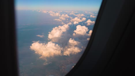 video shot through a plane window while flying over thick, puffy clouds after sunrise