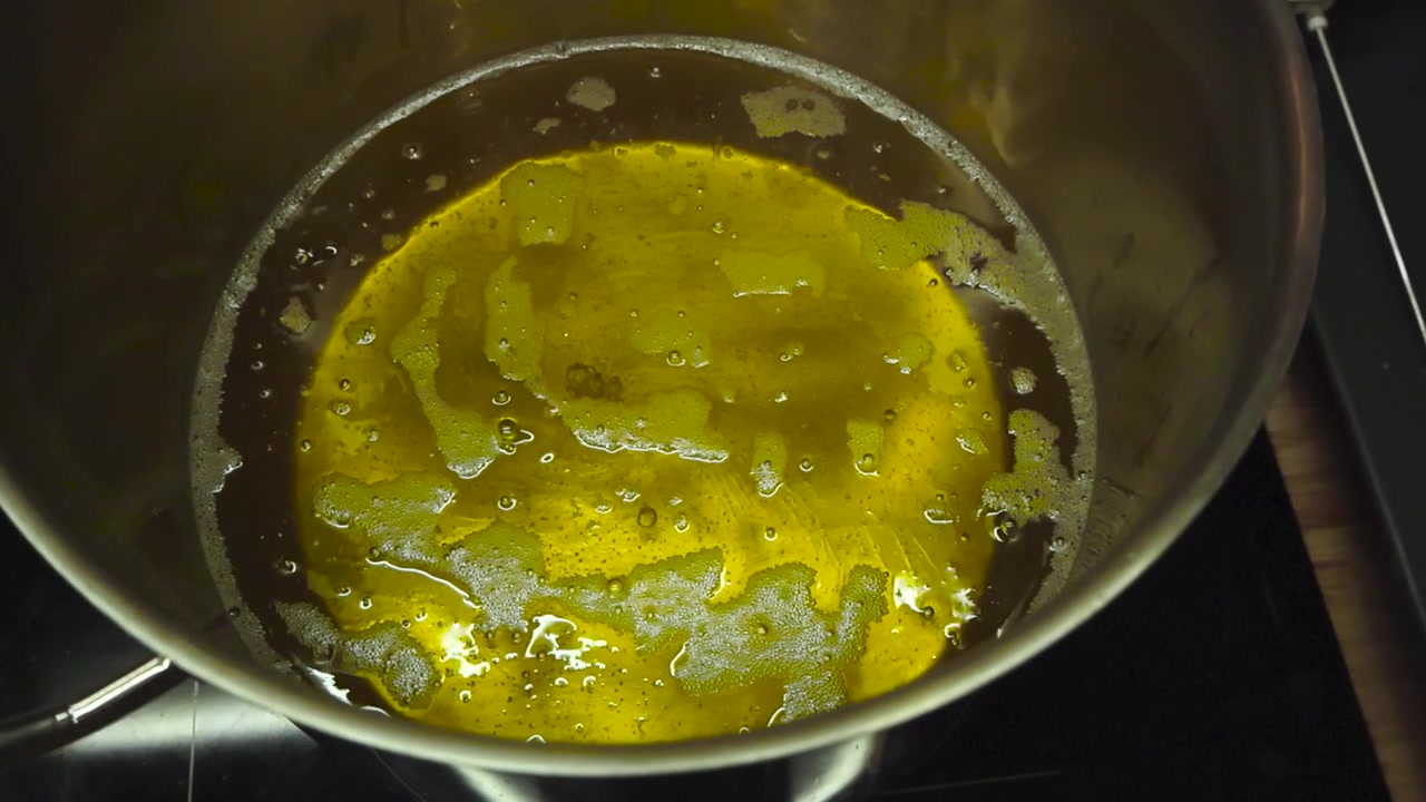 Óleo de fritadeira dourado em uma panela metálica cinza-aço, onde o óleo reflete nas laterais e ferve com bolhas estourando e girando na panela. O óleo está muito quente e pronto para cozinhar.