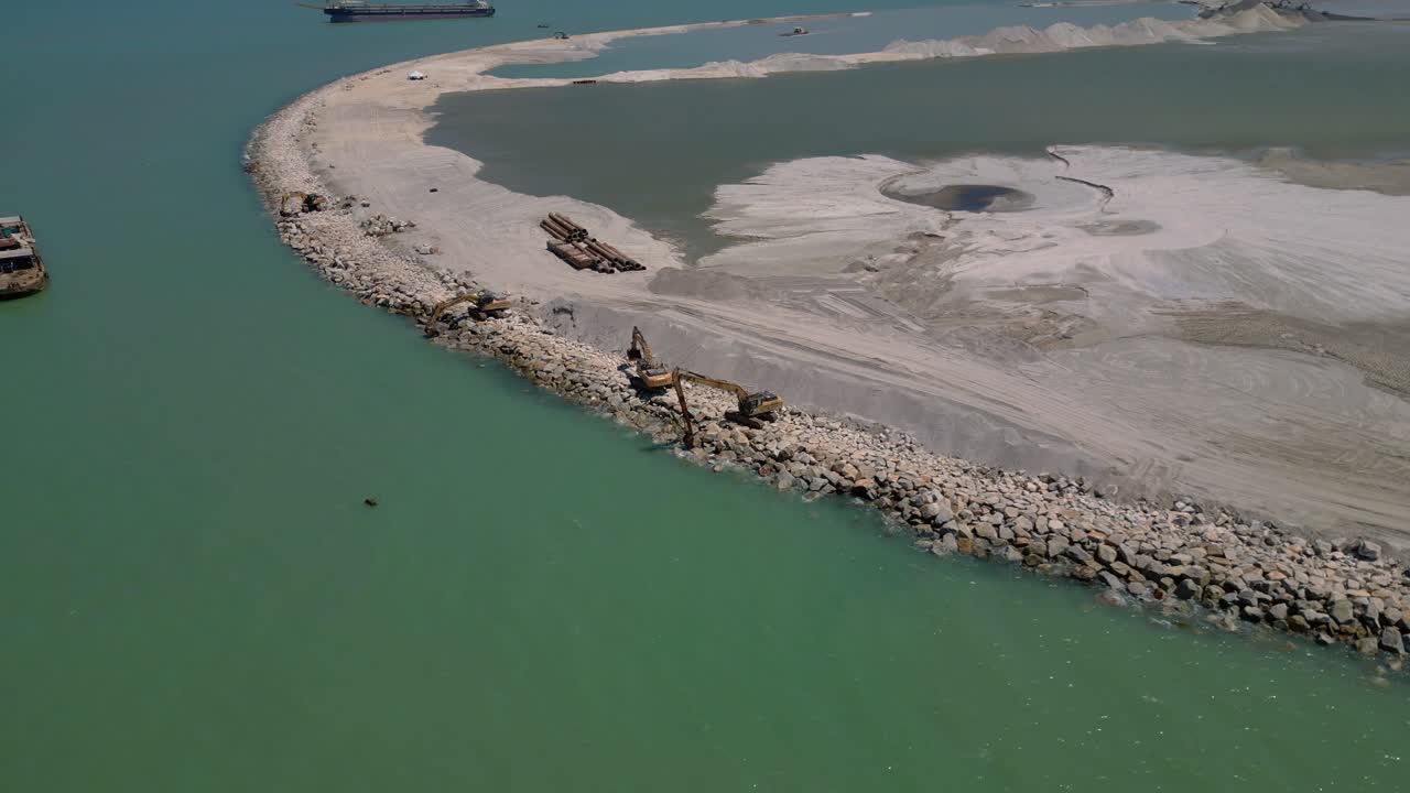 Escavatore di un progetto di ingegneria costiera che costruisce una nuova area terrestre dal mare con materiale roccioso e sabbia a Penangang. Splendida vista aerea dall'alto con drone.