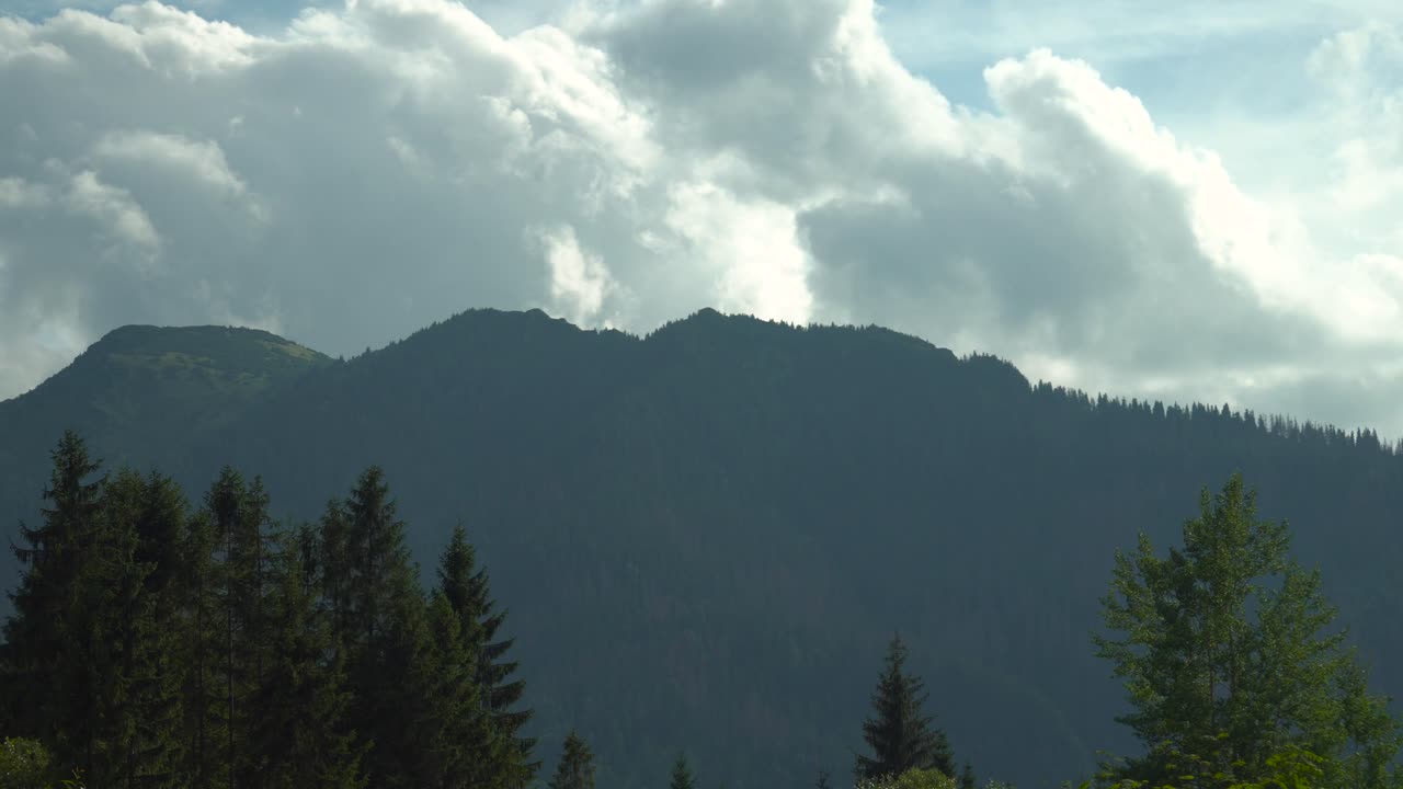 Timelapse di nuvole in rapido movimento su montagne scure e imponenti con alberi in primo piano
