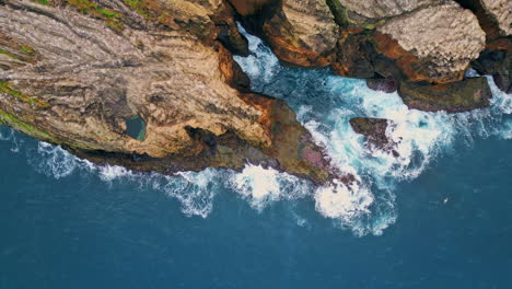 foaming waves crashing rocky cliffs top view. drone shot of dramatic coastline