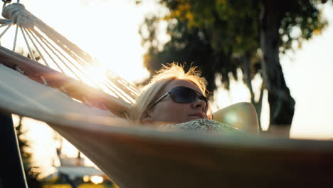 Una-Mujer-Turista-En-Un-Vestido-De-Verano-Se-Relaja-En-Una-Hamaca,-El-Sol-En-El-Horizonte-Crea-Hermosas-Altas