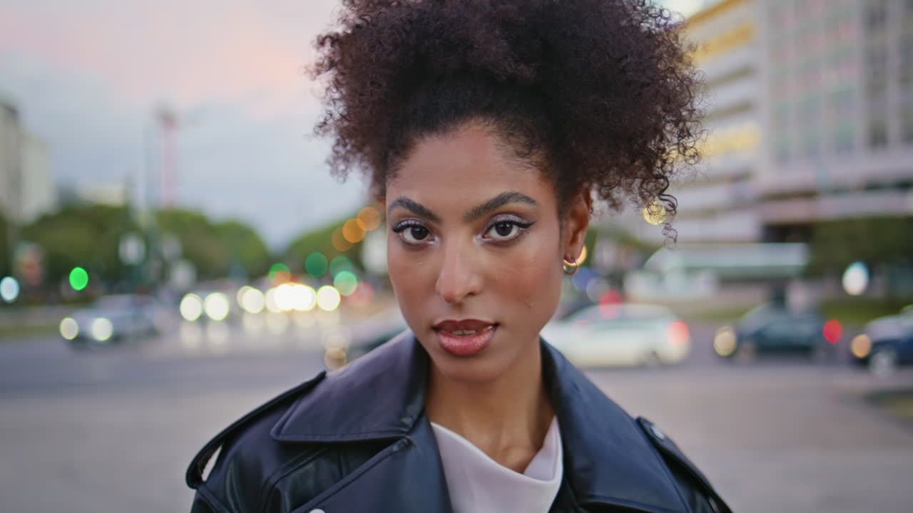 Fashionable girl looking camera standing in front twilight city lights closeup