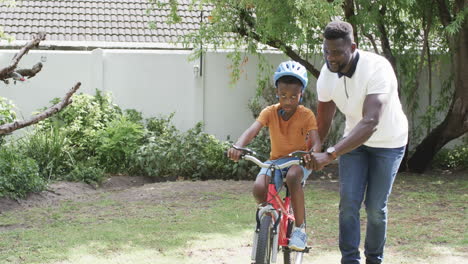 african american father teaches his son to ride a bike outdoors with copy space