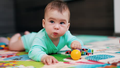 funny cute kid lies on belly holding a toy. sweet boy being playful and sticks out tongue. blurred backdrop.