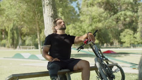 hombre cansado con pierna artificial sentado en un banco después de andar en bicicleta