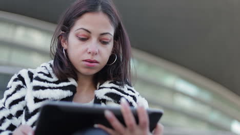 Nachdenkliche-Junge-Frau,-Die-Im-Freien-Auf-Ein-Tablet-Schaut