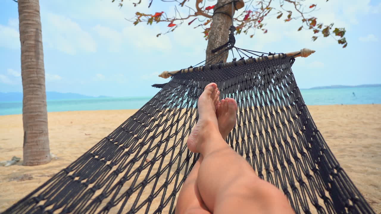 piernas desnudas en una hamaca en una playa de arena en una isla tropical, brisa ligera