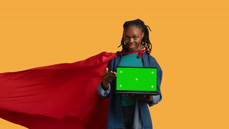 Portrait-of-jolly-teenager-acting-as-superhero-presenting-green-screen-laptop