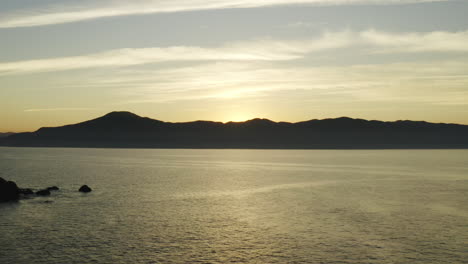 hermosa vista aérea de drones puesta de sol colores cálidos dorados sobre el océano y las montañas en el horizonte