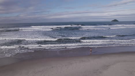 Drone-flying-up-at-the-shore-while-a-woman-walk-by-the-waves