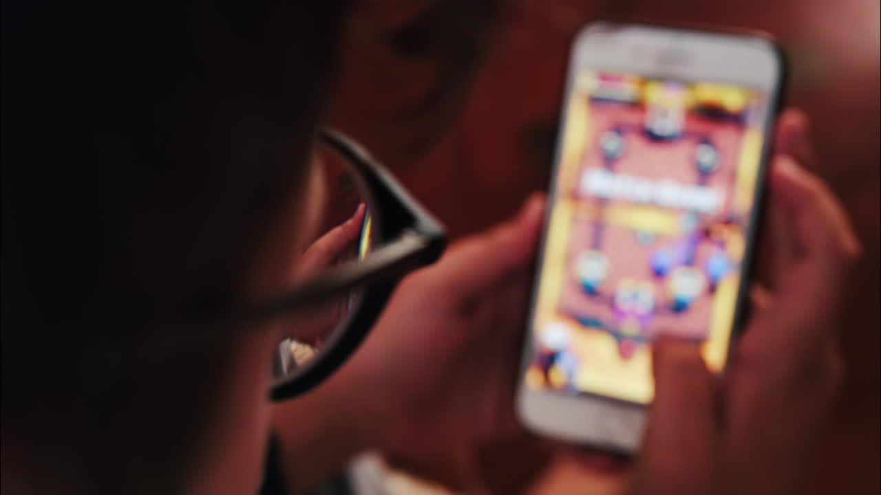 Over-the-shoulder close-up of a kid with glasses playing on a smartphone indoors