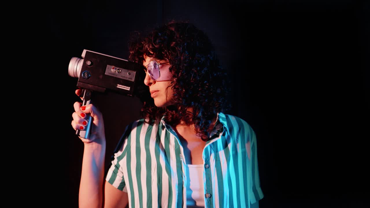Junge Frau richtet Vintage-Filmkamera in einem Studio mit Neonlichtern aus