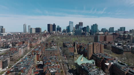 Residential-urban-neighbourhood-with-rows-of-multistorey-houses,-city-park-and-trunk-road.-Modern-downtown-skyscrapers-in-background.-Boston,-USA