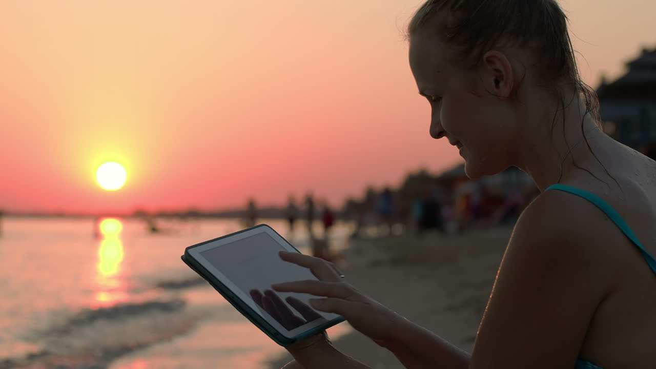 Donna felice con tablet in spiaggia al tramonto